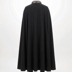 Op de afbeelding: Een zwarte cape tot op de grond met een gladde, donkerbruine kraag. Het kledingstuk wordt getoond op een etalagepop en heeft een volledig, vloeiend silhouet dat vanaf de schouders tot aan de zoom valt en de rug van de figuur bedekt.