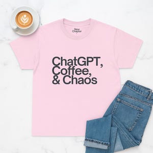 Puede incluir: Camiseta rosa claro con el texto negro "ChatGPT, Coffee, & Chaos". La imagen incluye vaqueros azules y una taza de café con arte latte. La camiseta tiene la inscripción "New Chapter" en el cuello.