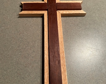 May include: A wooden cross with a dark brown center and light brown outer frame. The cross is made of two different types of wood.