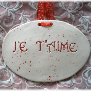 May include: White ceramic oval plaque with red splatter paint and the words "Je T'aime" in red.