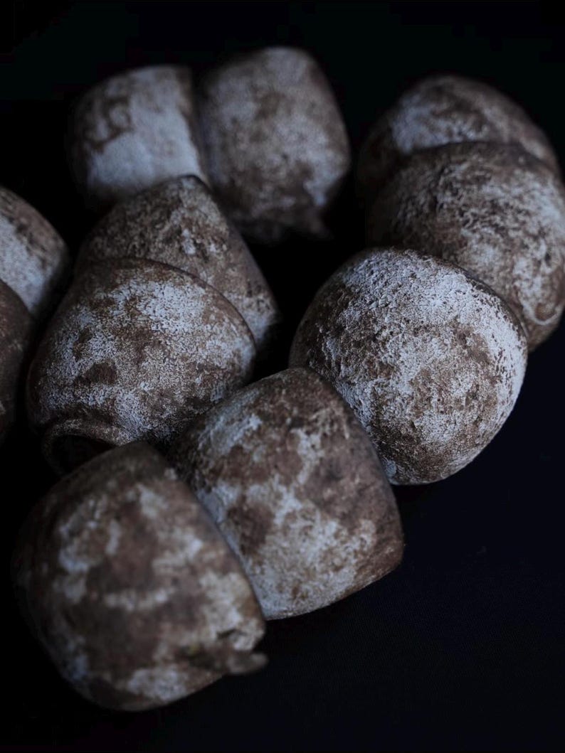 May include: Close-up of several brown, round pastries with a light dusting of white powder. The pastries are arranged closely together against a dark background, creating a contrast between the light and dark tones.