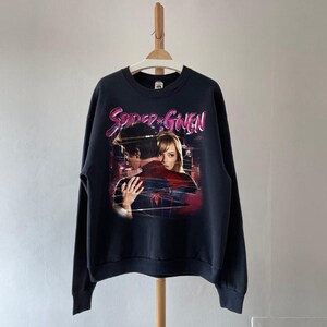 May include: A navy blue sweatshirt with a graphic of two people embracing, and the text "Spider & Gwen" in pink and white. The image has a vintage, faded appearance. The sweatshirt is hanging on a wooden hanger.