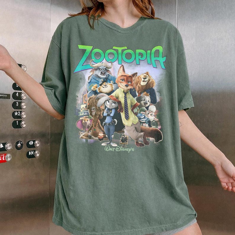 Puede incluir: Camiseta verde con la palabra "ZOOTOPIA" en verde y azul, y un gr&aacute;fico de personajes de la pel&iacute;cula animada. La camiseta es de cuello redondo.