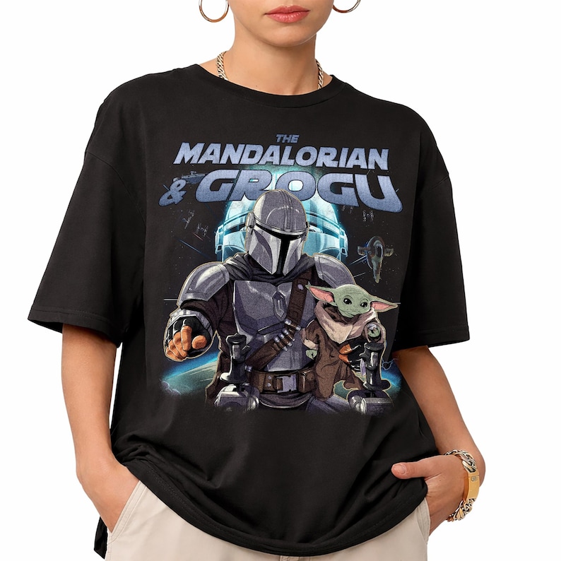 Może przedstawiać: Czarny t-shirt z grafiką The Mandalorian i Grogu z serii Star Wars. Projekt zawiera tekst "THE MANDALORIAN & GROGU" w kolorze niebieskim i białym, ze zdjęciami postaci i statku kosmicznego.