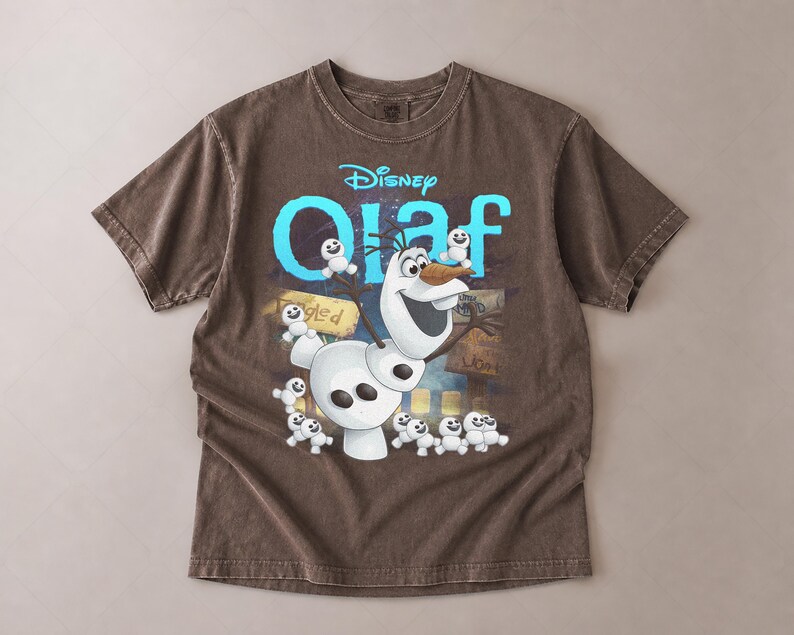 May include: Brown t-shirt featuring the Disney character Olaf from Frozen. The design includes Olaf, small snowmen, and the word "Olaf" in blue. The shirt has a vintage, washed look.