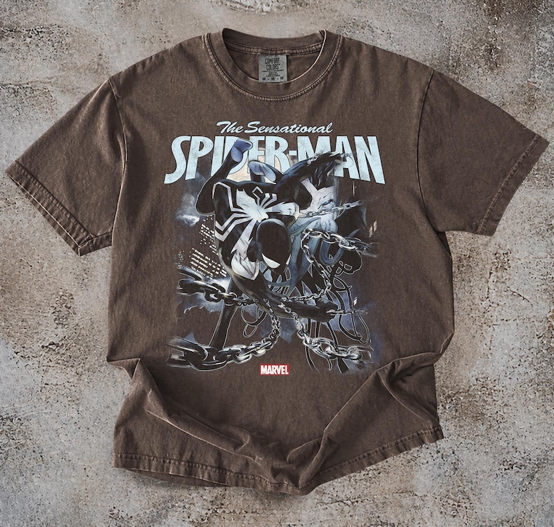May include: Brown t-shirt featuring a graphic of Spider-Man in black and white, with the text "The Sensational Spider-Man" in white. The Marvel logo is at the bottom. The shirt is made of a soft material.