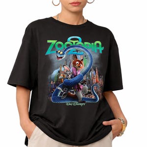 May include: Black t-shirt with a vibrant graphic from the film Zootopia. The design includes the film's title, a blue snake, and characters Judy Hopps and Nick Wilde. The Walt Disney's logo is also visible.