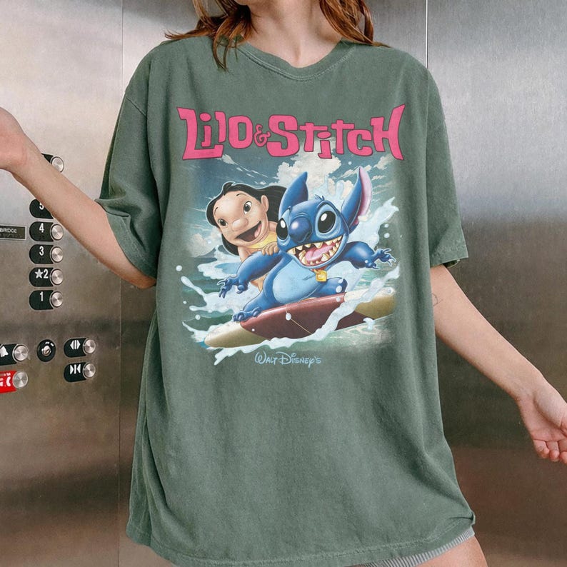 Peut inclure: T-shirt vert avec un imprim&eacute; de Lilo et Stitch surfant, avec l'inscription "Lilo & Stitch" en rose. Le design comprend &eacute;galement "Walt Disney's" en blanc. Le t-shirt est de coupe ample.