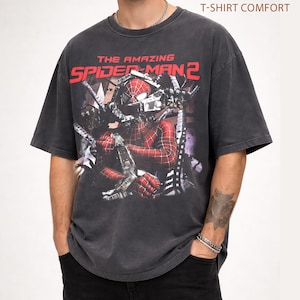 May include: Dark gray t-shirt featuring a distressed graphic of Spider-Man from "The Amazing Spider-Man 2." The design includes the movie title in red and a detailed image of the superhero. The shirt has short sleeves and a comfortable fit.