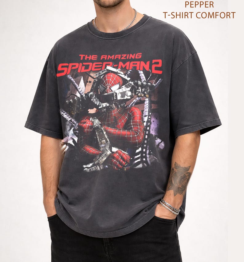 May include: Dark gray t-shirt featuring a distressed graphic of Spider-Man from "The Amazing Spider-Man 2." The design includes the movie title in red and a detailed image of the superhero. The shirt has short sleeves and a comfortable fit.