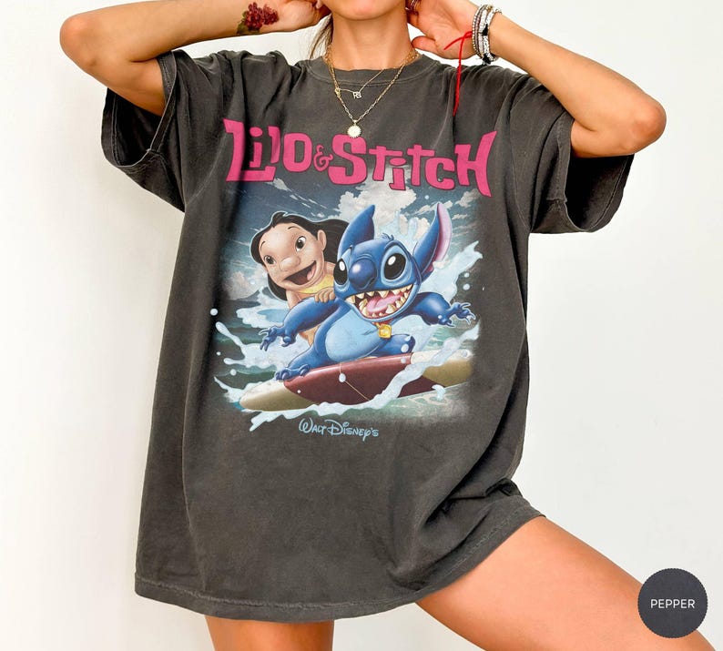Peut inclure: T-shirt gris fonc&eacute; avec les personnages Lilo et Stitch. Le graphisme montre Lilo et Stitch surfant sur une vague, avec les mots "Lilo & Stitch" en rose. Le logo Walt Disney est en bas.