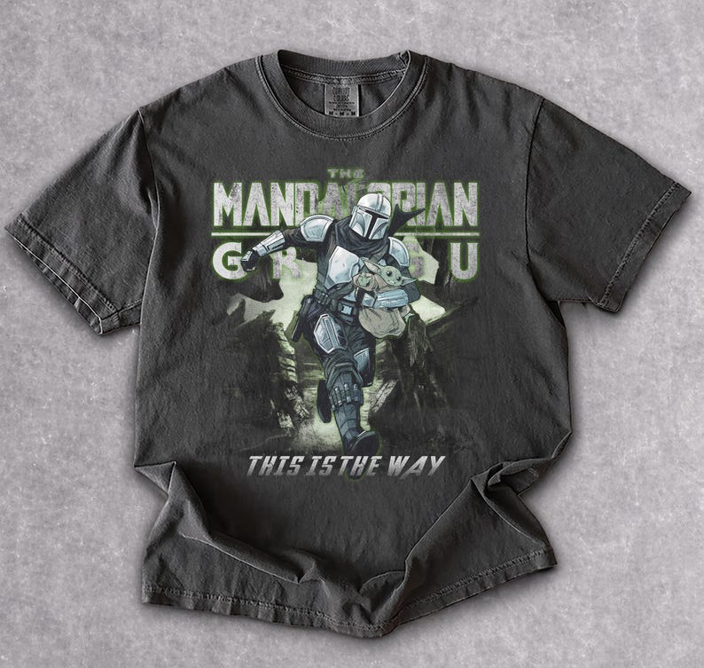 Puede incluir: Camiseta gris oscuro con un gr&aacute;fico de The Mandalorian y Grogu. El texto "THE MANDALORIAN" est&aacute; encima de la imagen, con "THIS IS THE WAY" debajo. El dise&ntilde;o est&aacute; impreso en una camiseta de manga corta y cuello redondo.