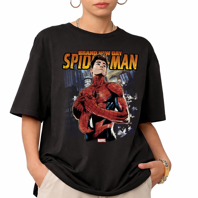 Pu&ograve; includere: T-shirt nera con grafica di Spider-Man in rosso e blu, con le parole "BRAND NEW DAY SPIDER-MAN" in giallo. Il logo Marvel &egrave; visibile. La maglietta &egrave; indossata da una persona.
