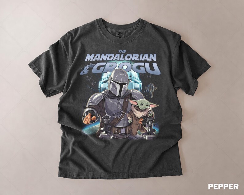 Może przedstawiać: Ciemnoszara koszulka z grafiką The Mandalorian i Grogu z serii Star Wars. Projekt zawiera tekst "The Mandalorian & Grogu" w kolorze niebieskim i białym, z ilustracjami postaci.