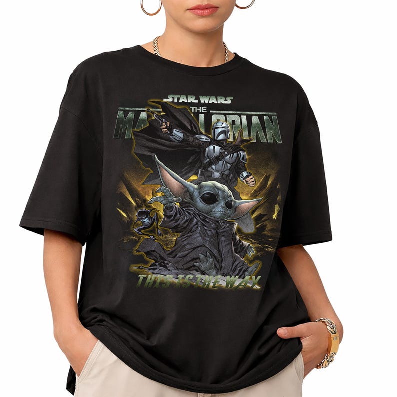 May include: Black t-shirt featuring a graphic from the Star Wars series, The Mandalorian. The design includes the Mandalorian, Grogu, and the text "This is the Way" in a yellow and green color scheme.