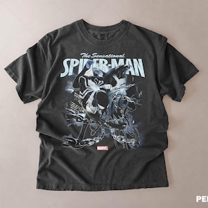 May include: Dark gray t-shirt featuring a graphic of Spider-Man with the text "The Sensational Spider-Man" in white. The Marvel logo is at the bottom. The shirt has a vintage, distressed look.