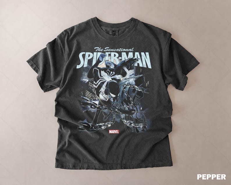 May include: Dark gray t-shirt featuring a graphic of Spider-Man with the text "The Sensational Spider-Man" in white. The Marvel logo is at the bottom. The shirt has a vintage, distressed look.