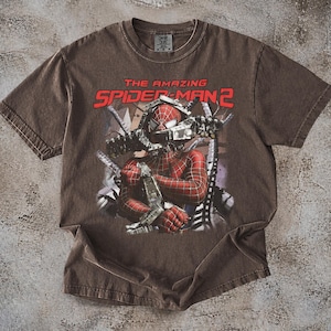 May include: Brown t-shirt featuring a graphic of Spider-Man from "The Amazing Spider-Man 2." The design shows Spider-Man in his red and black suit, with the movie title in red letters. The shirt has a vintage, worn look.