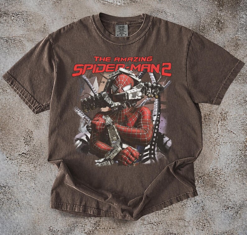 May include: Brown t-shirt featuring a graphic of Spider-Man from "The Amazing Spider-Man 2." The design shows Spider-Man in his red and black suit, with the movie title in red letters. The shirt has a vintage, worn look.
