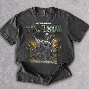 May include: Dark gray t-shirt featuring a graphic from the Star Wars series, "The Mandalorian." The design includes characters like the Mandalorian and Grogu, with the text "This is the Way."
