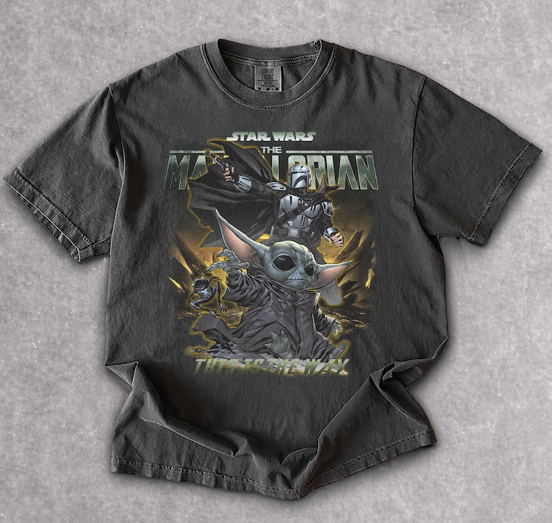 May include: Dark gray t-shirt featuring a graphic from the Star Wars series, "The Mandalorian." The design includes characters like the Mandalorian and Grogu, with the text "This is the Way."