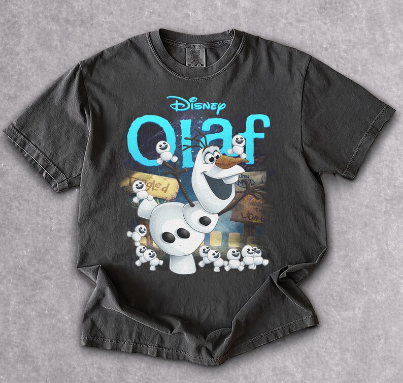 May include: Dark gray t-shirt featuring the Disney character Olaf from Frozen. The design includes Olaf, small snowmen, and the word "Olaf" in blue. The shirt is made of a soft material.