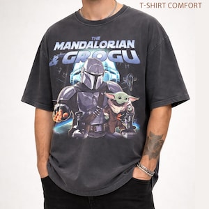 Może przedstawiać: Ciemnoszara koszulka z grafiką "The Mandalorian & Grogu". Projekt przedstawia Mandalorianina i Grogu. Tekst "Pepper T-Shirt Comfort" znajduje się na g&oacute;rze koszulki.