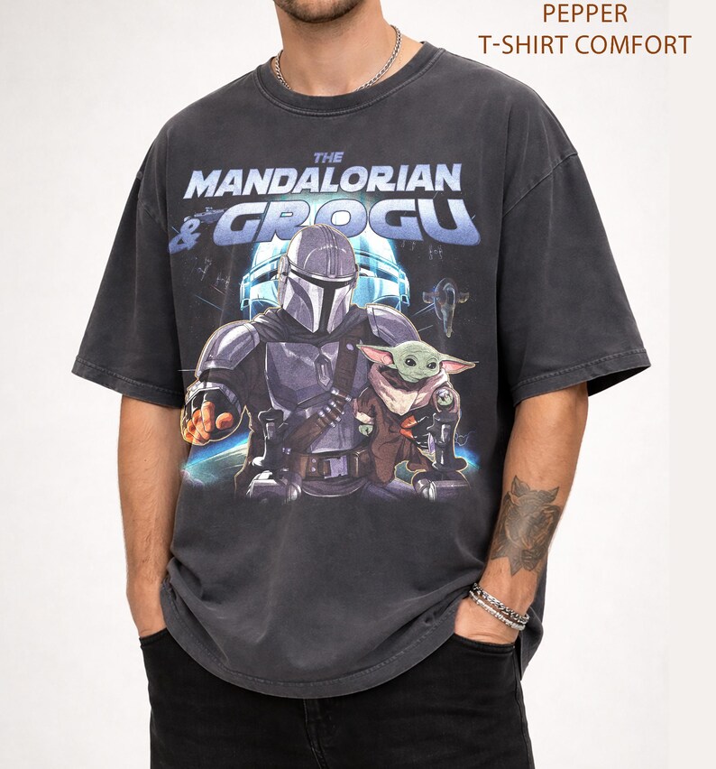 Może przedstawiać: Ciemnoszara koszulka z grafiką "The Mandalorian & Grogu". Projekt przedstawia Mandalorianina i Grogu. Tekst "Pepper T-Shirt Comfort" znajduje się na g&oacute;rze koszulki.