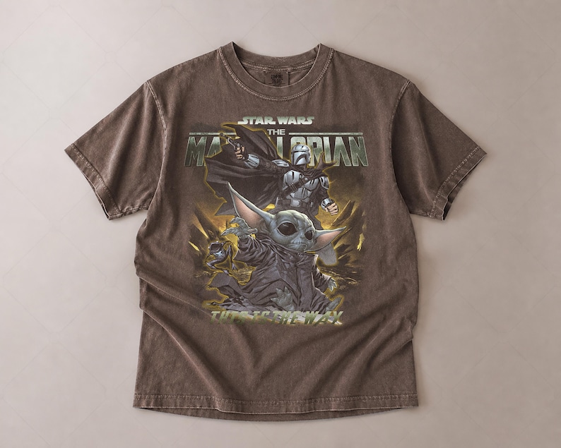 May include: Brown Star Wars The Mandalorian t-shirt featuring a graphic of The Mandalorian and Grogu. The text "STAR WARS THE MANDALORIAN" is printed across the top. The shirt is made of a soft, comfortable material.