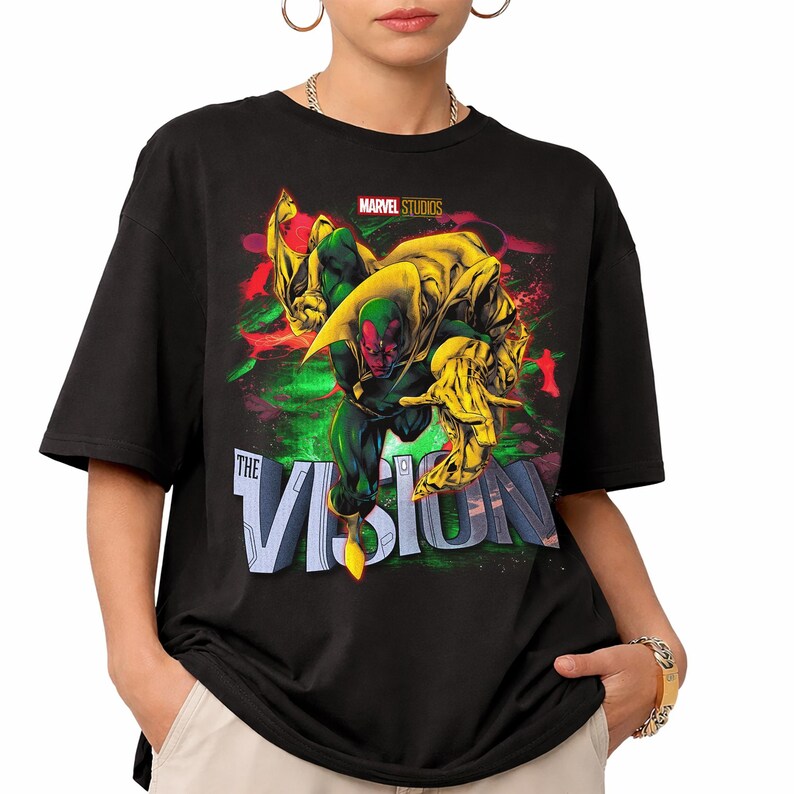 Puede incluir: Camiseta negra con un gr&aacute;fico del personaje Vision de Marvel Studios. El dise&ntilde;o incluye a Vision en verde y rojo, con detalles amarillos, y el texto "THE VISION". El logotipo de Marvel Studios est&aacute; en la parte superior.