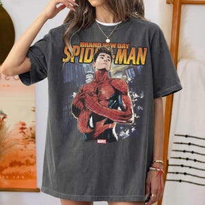 Pu&ograve; includere: T-shirt grigio scuro con grafica di Spider-Man e la scritta "BRAND NEW DAY SPIDER-MAN" in giallo e arancione. Il logo Marvel &egrave; in basso. La maglietta ha un aspetto vintage.