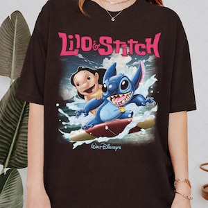 Peut inclure: T-shirt marron fonc&eacute; avec l'inscription rose "Lilo & Stitch". Le graphisme repr&eacute;sente Lilo et Stitch surfant sur une vague. Le logo Walt Disney's est en bas de l'image.