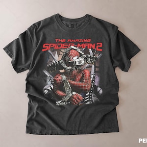 May include: A dark gray t-shirt featuring a graphic from "The Amazing Spider-Man 2". The design shows Spider-Man in his costume with mechanical arms. The text "THE AMAZING SPIDER-MAN 2" is printed in red across the top.