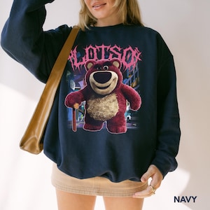 K&ouml;nnte beinhalten: Marineblaues Sweatshirt mit einem Aufdruck von Lotso, einem roten B&auml;ren, und dem Wort "LOTSO" in rosa Schrift. Der B&auml;r h&auml;lt einen kleinen Stock. Das Sweatshirt hat eine marineblaue Farbe.