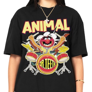 Könnte beinhalten: Ein schwarzes T-Shirt mit einem Grafikdruck der Muppet-Figur Animal, die Schlagzeug spielt. Das Wort ANIMAL ist oben in großen gelben Buchstaben gedruckt, und die Worte DR. TEETH stehen in gelber Schrift auf der Bassdrum.