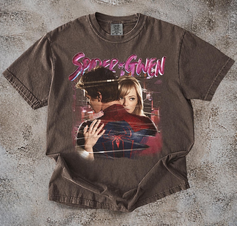 May include: Brown t-shirt with a graphic of Spider-Man and Gwen Stacy, and the text "Spider-Gwen" in pink and purple. The shirt has a vintage, distressed appearance.