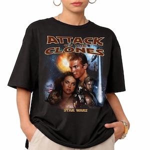 May include: Black t-shirt with the movie poster for "Star Wars: Attack of the Clones." The design features the film's title in brown lettering, and images of the main characters set against a space-themed backdrop.