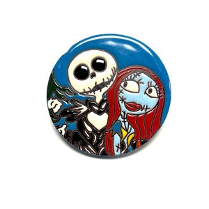 May include: A round, blue pin featuring Jack Skellington and Sally from The Nightmare Before Christmas. Jack is a white skeleton in a black suit, and Sally has blue skin and red hair. The pin has a glossy finish.