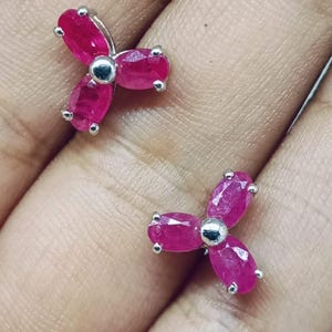 Op de afbeelding: Een paar bloemvormige oorstekers. Elke oorbel heeft drie ovale, helder roze edelstenen gezet in zilverkleurig metaal. De oorbellen worden getoond op een lichtgekleurd oppervlak. De tekst "MONDAL GEMS" is zichtbaar.