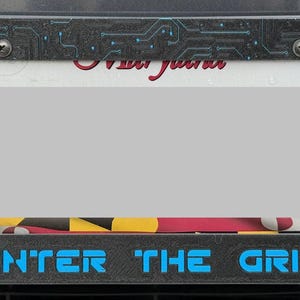 May include: License plate frame with a black and gray circuit board design. The frame has the text "ENTER THE GRID" in blue. The top of the frame has the text "Maryland" in red script.