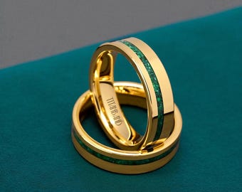 May include: Two gold wedding bands with a vibrant green inlay. The rings are stacked, showcasing the polished gold and the textured green stone. The text "TITANS BAND" is engraved on the inside of one ring.