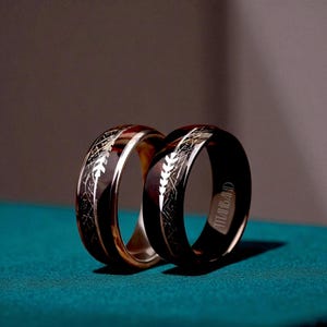 May include: Two rings with a black and silver design. One ring is silver with a black interior, and the other is black with a silver interior. Both rings have a feather-like pattern and the word "TITANBAND" engraved on the inside.