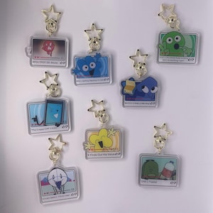 Può includere: Una collezione di portachiavi in acrilico trasparente con personaggi dei cartoni animati e testo. Ogni portachiavi ha una chiusura dorata a forma di stella. I portachiavi mostrano vari personaggi e frasi, tra cui "Alone", "The Crappy Cliff" e "X Finds Out His Value".