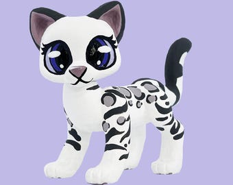 Könnte beinhalten: Eine weiße Katzenfigur mit schwarzen und grauen Flecken und Streifen. Die Katze hat große blaue Augen, schwarze Ohren und einen schwarzen Schwanz. Die Figur steht auf allen Vieren.