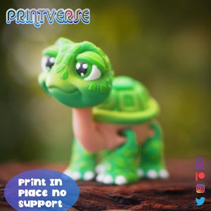 May include: A green and tan turtle figurine with a friendly face and patterned shell. The figurine is on a wooden surface. The text "PRINTVERSE" is at the top, and "Print in Place no support" is at the bottom. The turtle has large eyes.