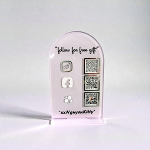 Op de afbeelding: Een heldere, boogvormige acryl displaystandaard met de tekst "follow for free gift" en social media-iconen. De standaard heeft QR-codes voor Instagram, Facebook en andere platforms, samen met de gebruikersnaam "xxNguyenKitty".