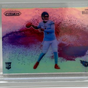 Könnte beinhalten: Eine Cam Ward Football-Sammelkarte in einer Schutzhülle. Die Karte zeigt einen Spieler in blauem Trikot beim Werfen eines Footballs, mit dem Logo "Panini Prizm" oben. Der Hintergrund hat ein farbenfrohes, abstraktes Design.