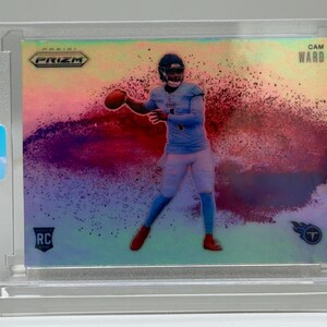 May include: A Cam Ward football trading card in a protective case. The card features a player in a light blue uniform throwing a football, with a colorful, abstract background. The card is labeled "RC" and "Prizm."