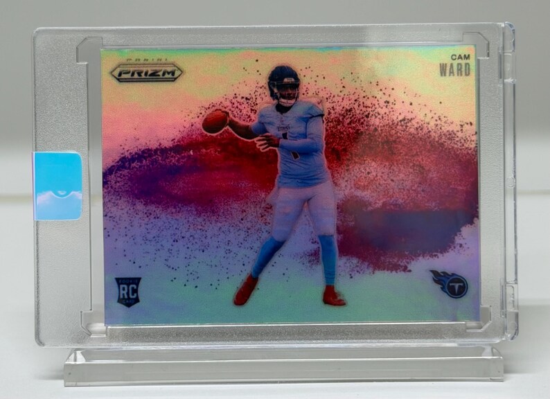 May include: A Cam Ward football trading card in a protective case. The card features a player in a light blue uniform throwing a football, with a colorful, abstract background. The card is labeled "RC" and "Prizm."