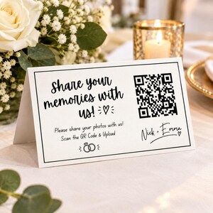 May include: A white folded card with black text reading Share your memories with us! Please share your photos with us! Scan the QR Code & Upload, featuring a QR code, a heart icon, wedding ring icons, and the names Nick + Emma.